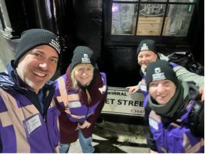 Four people in Street Angels Birkenhead uniform smile from in front of a road sign.